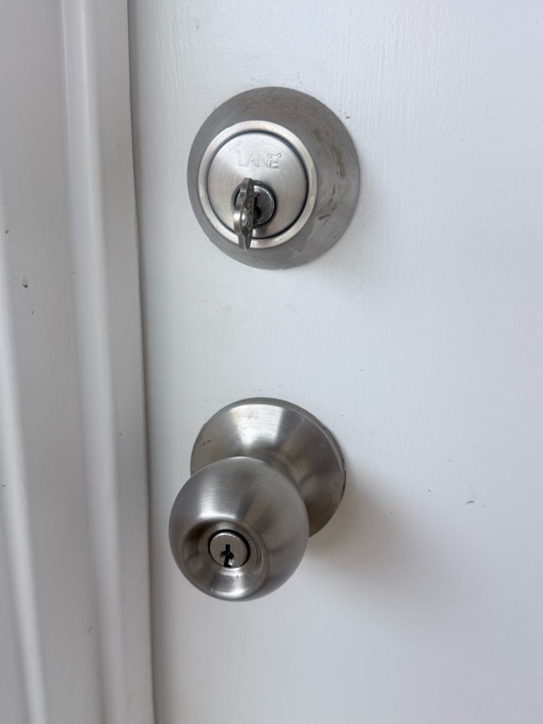 Lane deadbolt with key inserted above a knob lock on a white storeroom door