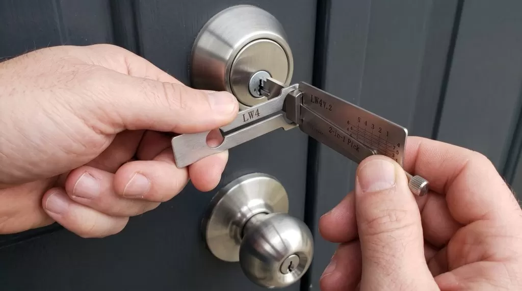 Illustration: a locksmith's hands using a Lishi pick on a deadbolt above a knob set on a charcoal door