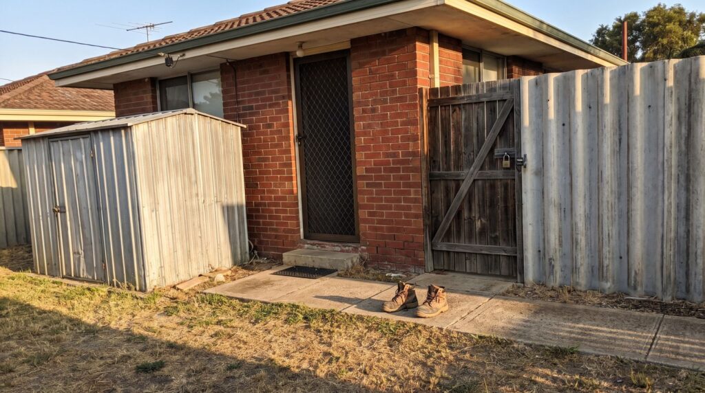 A brick house with a security screen door, a timber side gate and a garden shed