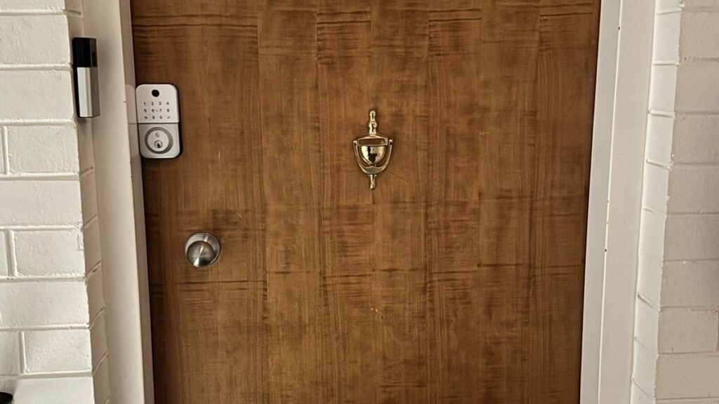 A timber front door with a deadbolt, a knob and a brass door knocker